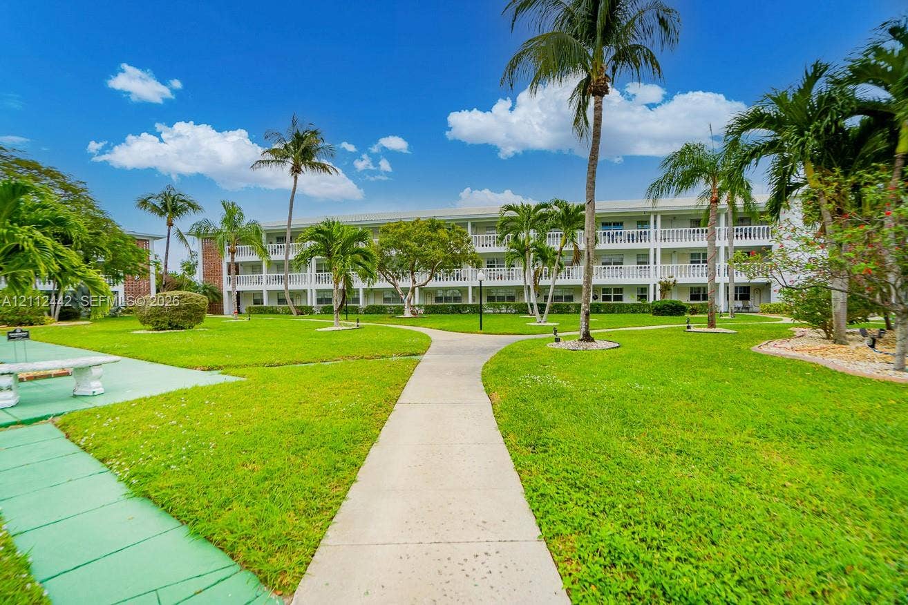 2455 NE 51st Street, #E114, Fort Lauderdale, FL 33308 Expansive green space featuring mature palm trees, manicured landscaping, concrete pathways, and a multi-story building with exterior balconies
