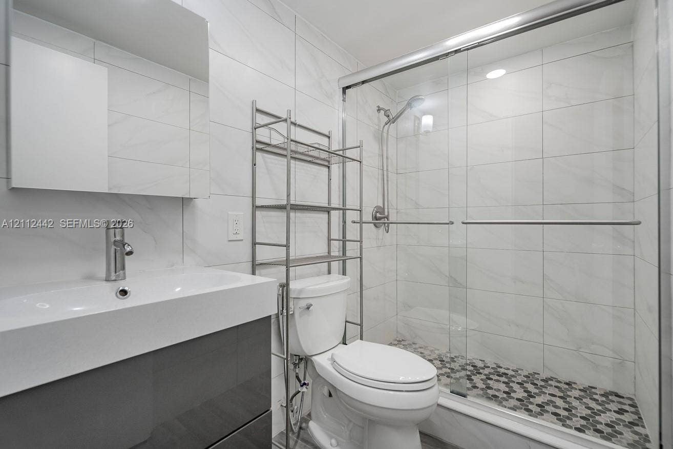 2455 NE 51st Street, #E114, Fort Lauderdale, FL 33308 Bathroom featuring a vanity with an integrated rectangular sink, wall-mounted mirror, glass-enclosed shower with a handheld fixture, and tiled surfaces