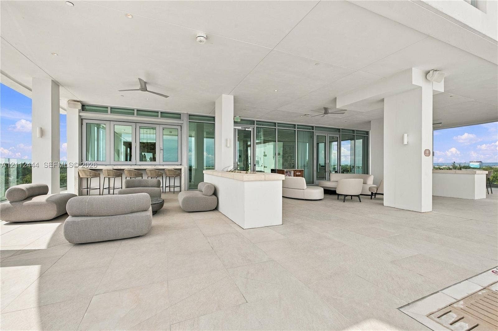 Covered terrace featuring large-format stone tile flooring, built-in stone bar counter, floor-to-ceiling glass paneling, and ceiling-mounted fans