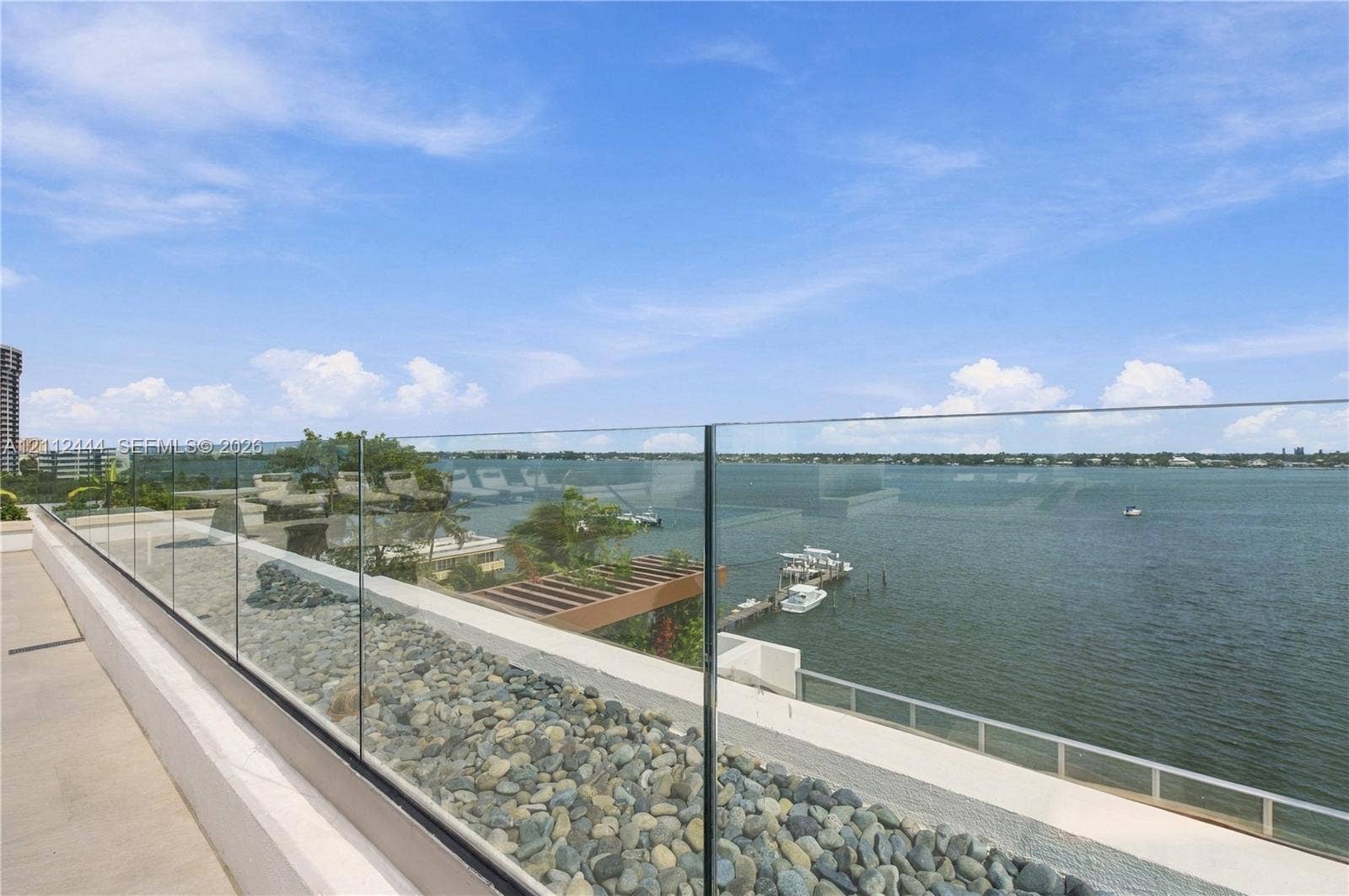 Elevated balcony featuring a frameless glass railing, stone-finished flooring, and water frontage