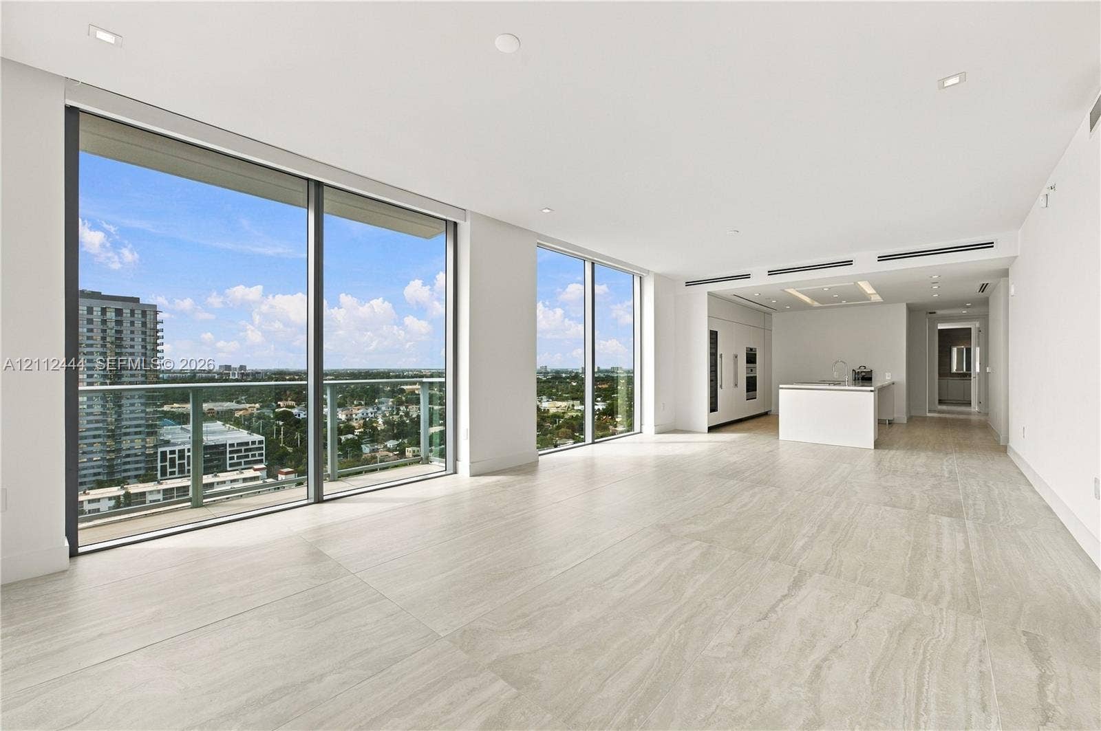 Floor-to-ceiling glass windows, expansive stone-finish flooring, recessed lighting, integrated kitchen appliances, and a minimalist stone-top island