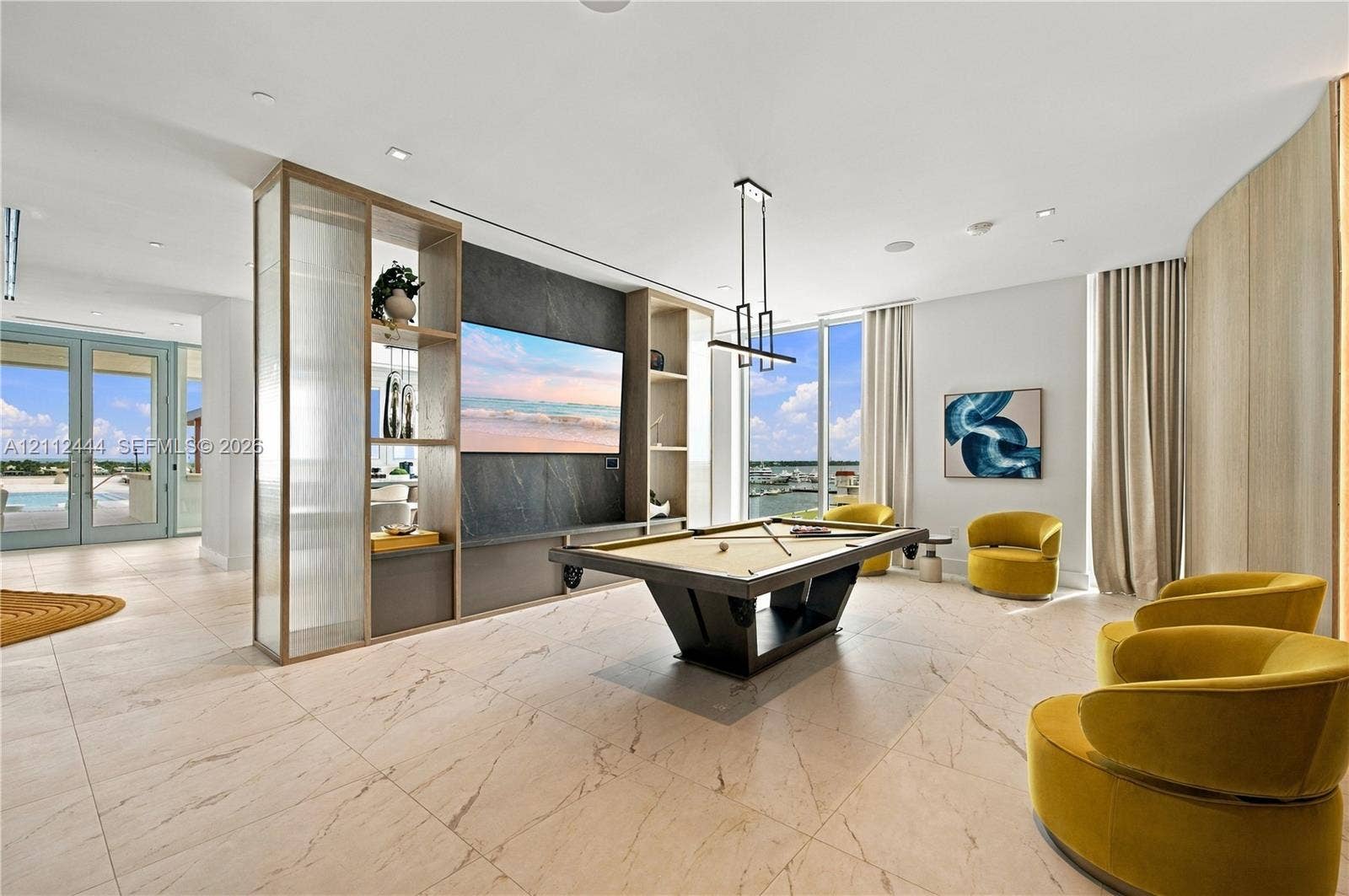 Open-concept space featuring large-format tile flooring, floor-to-ceiling windows, a custom stone-clad media wall with built-in shelving, and recessed ceiling lighting