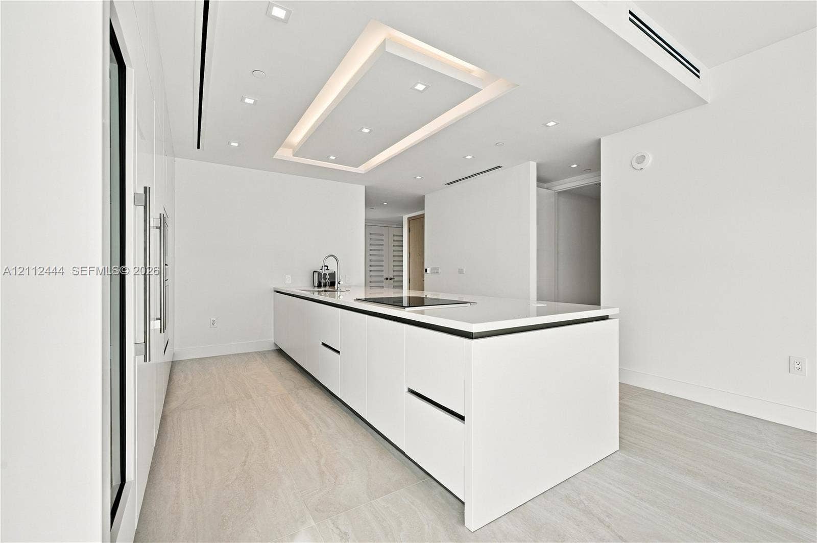 Minimalist kitchen featuring matte white flat-panel cabinetry, a quartz waterfall-edge island, an integrated induction cooktop, recessed lighting, and stone-finish tile flooring