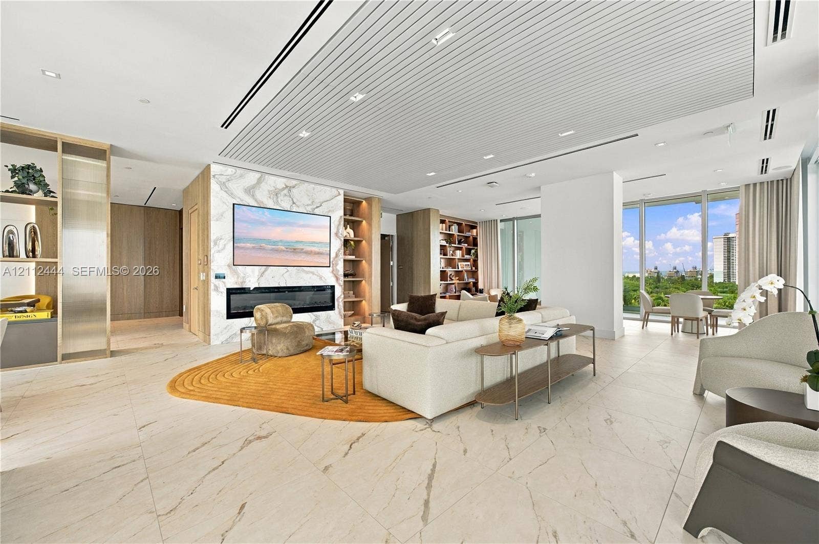 Open-concept interior featuring large-format tile flooring, a floor-to-ceiling stone-clad fireplace wall, custom built-in shelving, a tiered slatted ceiling with recessed lighting, and floor-to-ceiling windows