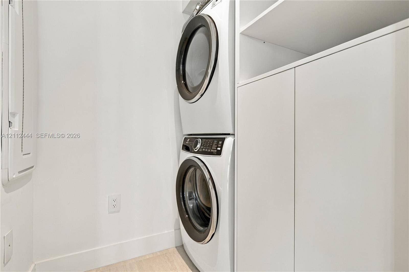 Laundry area featuring a stackable front-load washer and dryer, integrated white cabinetry with open shelving, and light-toned flooring