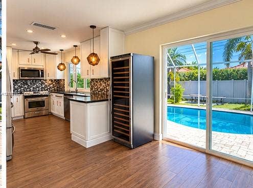 Kitchen featuring white shaker-style cabinetry, dark stone countertops, stainless steel appliances, built-in wine storage, and wood-finish flooring