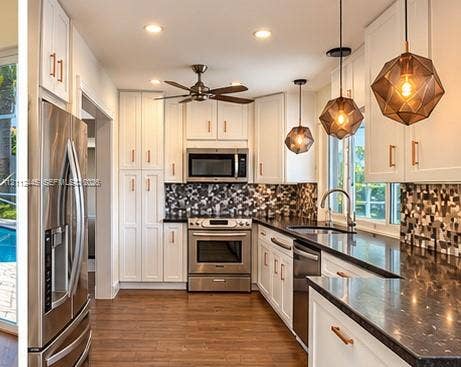 Kitchen featuring white cabinetry with metallic hardware, dark stone-finish countertops, geometric glass pendant lighting, and stainless steel appliances
