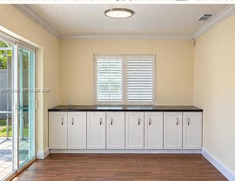 Custom built-in white cabinetry featuring dark stone-finish countertops, wood-finish flooring, sliding glass door, and window with plantation-style shutters