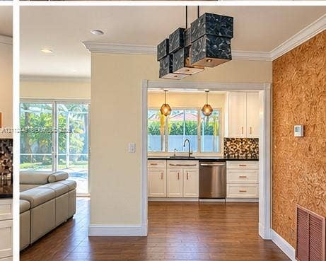 Multi-light geometric chandelier, wood-finish flooring, crown molding, kitchen with white cabinetry, and textured wood-panel wall feature