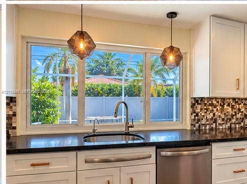 Kitchen featuring white cabinetry with metallic hardware, dark countertops, a mosaic tile backsplash, stainless steel sink with high-arc faucet, and geometric pendant lighting