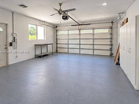 Spacious garage featuring a durable epoxy floor finish, wall-mounted storage cabinetry, recessed lighting, and a ceiling fan