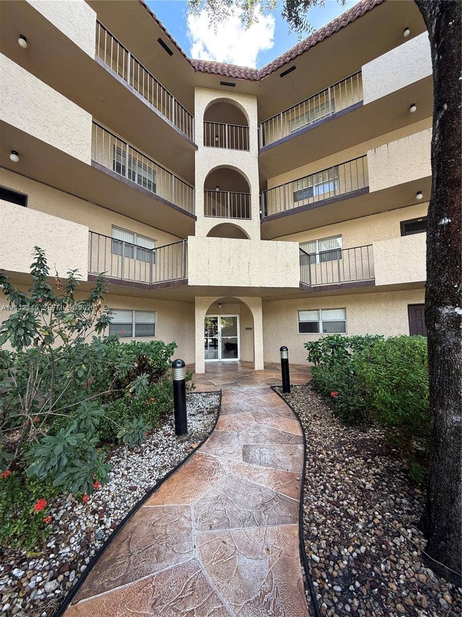 6100 S Falls Cir Drive, #411, Lauderhill, FL 33319 Multi-story stucco exterior featuring arched architectural detailing, private balconies with metal railings, a tiled roofline, and a flagstone walkway