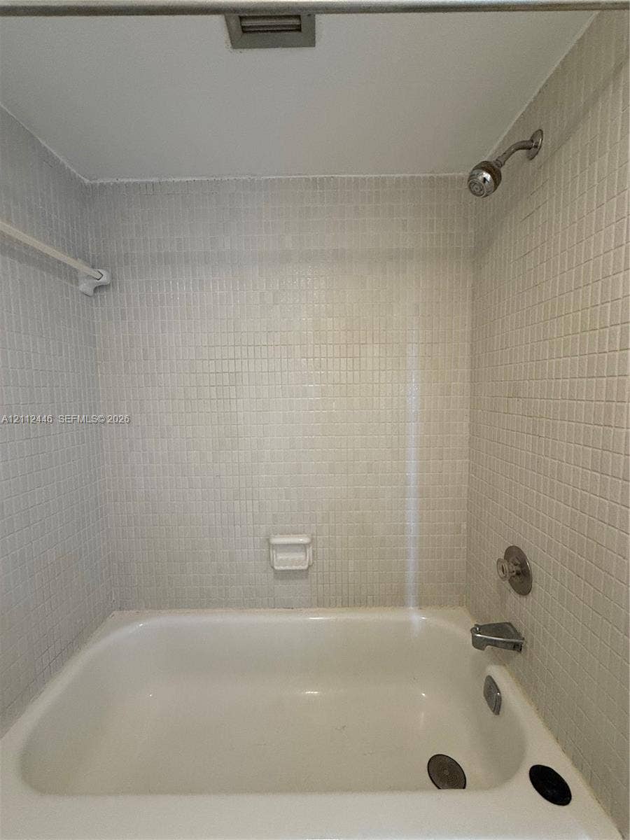 6100 S Falls Cir Drive, #411, Lauderhill, FL 33319 Bathtub featuring a white finish, wall-mounted shower head, integrated faucet, built-in soap dish, and neutral mosaic tile surround