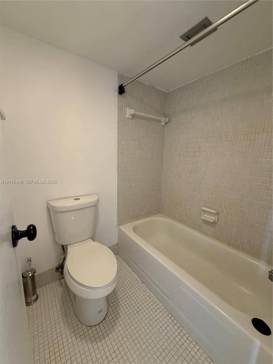 6100 S Falls Cir Drive, #411, Lauderhill, FL 33319 Bathroom featuring a white bathtub, small-format tile flooring, wall-mounted shower curtain rod, and integrated soap dish