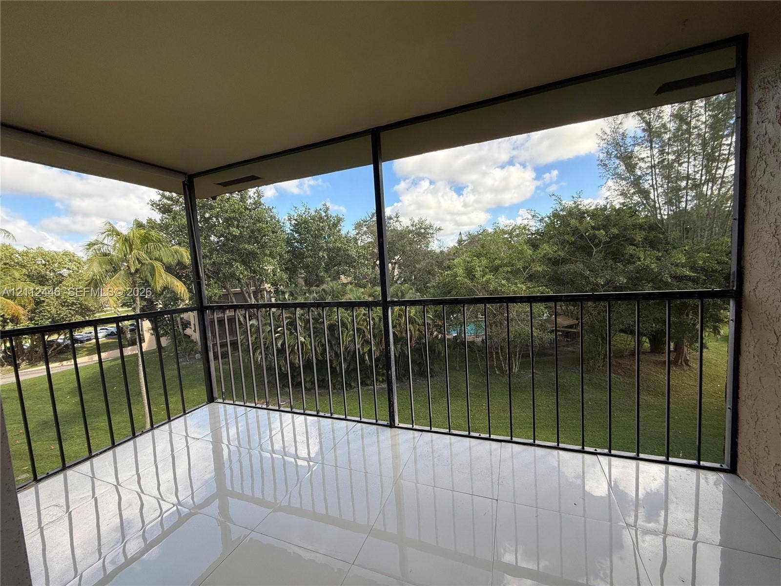 6100 S Falls Cir Drive, #411, Lauderhill, FL 33319 Screened-in balcony featuring white tile flooring, black metal railing, and a textured stucco ceiling