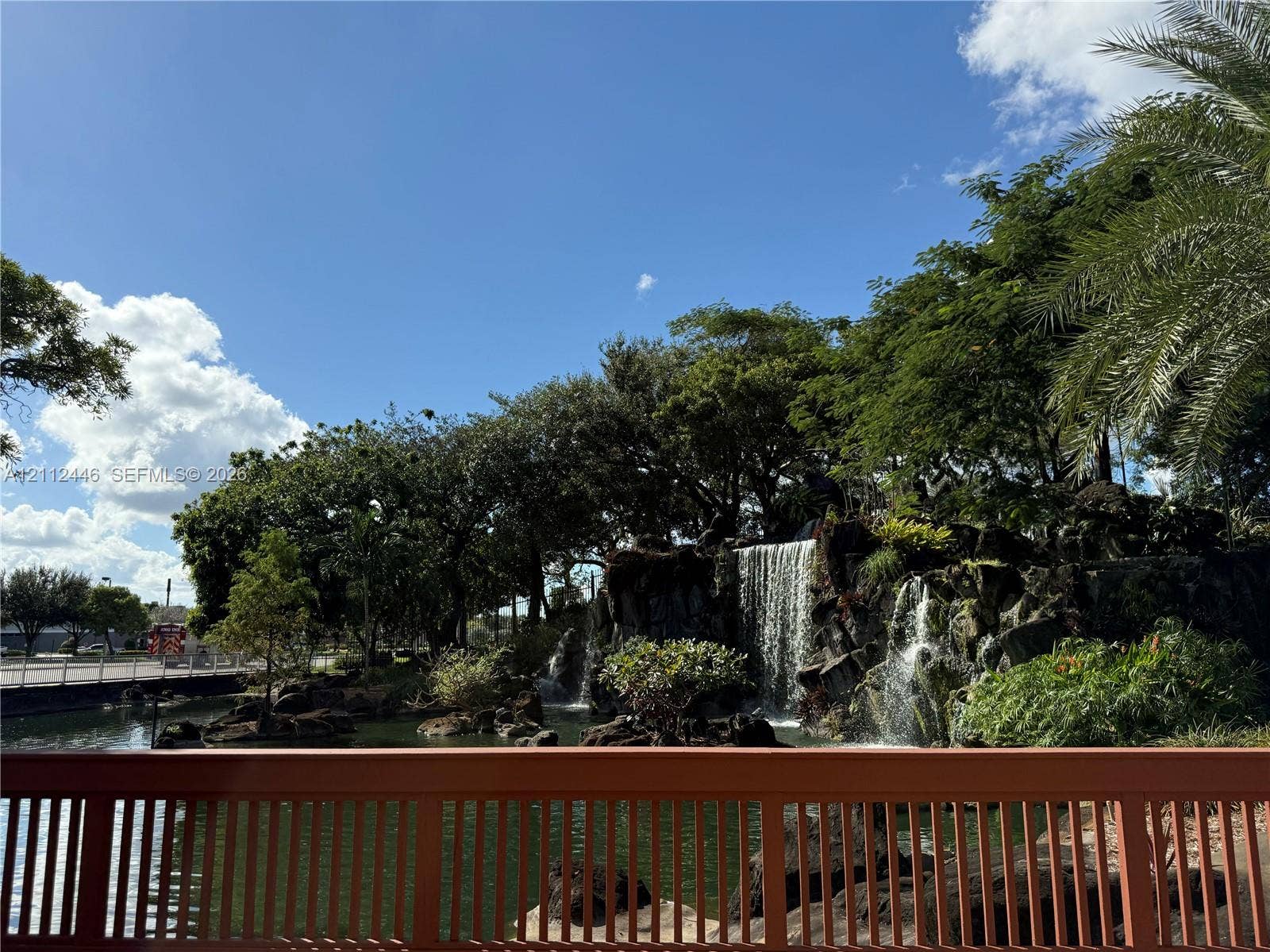 6100 S Falls Cir Drive, #411, Lauderhill, FL 33319 Custom rock-scaped waterfall with tiered water features, built-in stone retaining wall, mature landscaping, and an ornamental metal railing overlooking the water