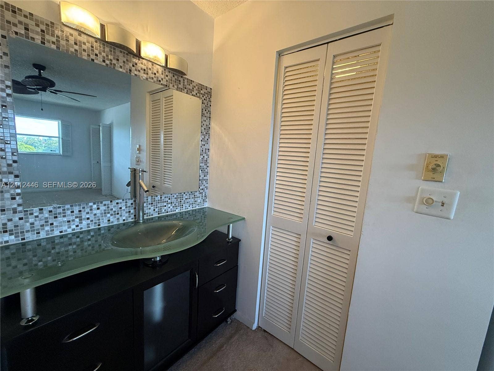 6100 S Falls Cir Drive, #411, Lauderhill, FL 33319 Black vanity featuring a glass vessel sink, chrome single-lever faucet, tiled mirror surround, and louvered bi-fold closet doors
