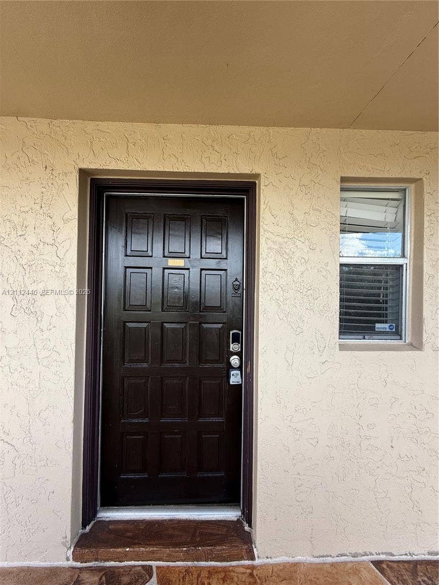 6100 S Falls Cir Drive, #411, Lauderhill, FL 33319 Dark-finished multi-panel entry door with electronic deadbolt, textured stucco exterior, and window with integrated blinds