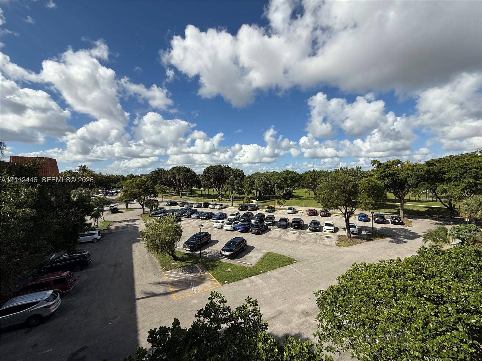 6100 S Falls Cir Drive, #411, Lauderhill, FL 33319 Asphalt-paved parking lot with dedicated parking spaces, bordered by mature trees and landscaped green areas