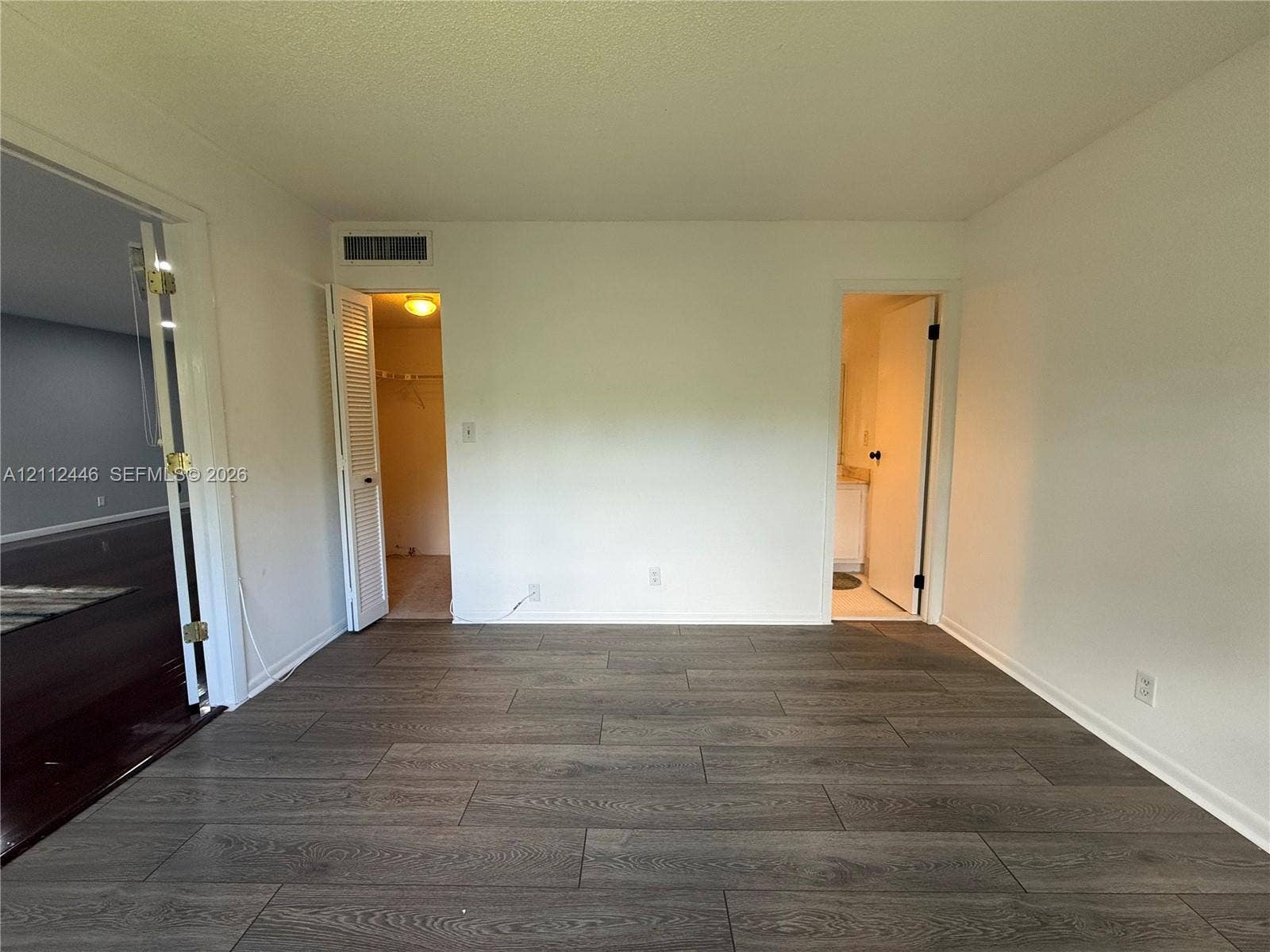 6100 S Falls Cir Drive, #411, Lauderhill, FL 33319 Neutral-toned interior space featuring wood-finish flooring, two doorway entries, a louvered closet door, and a textured ceiling