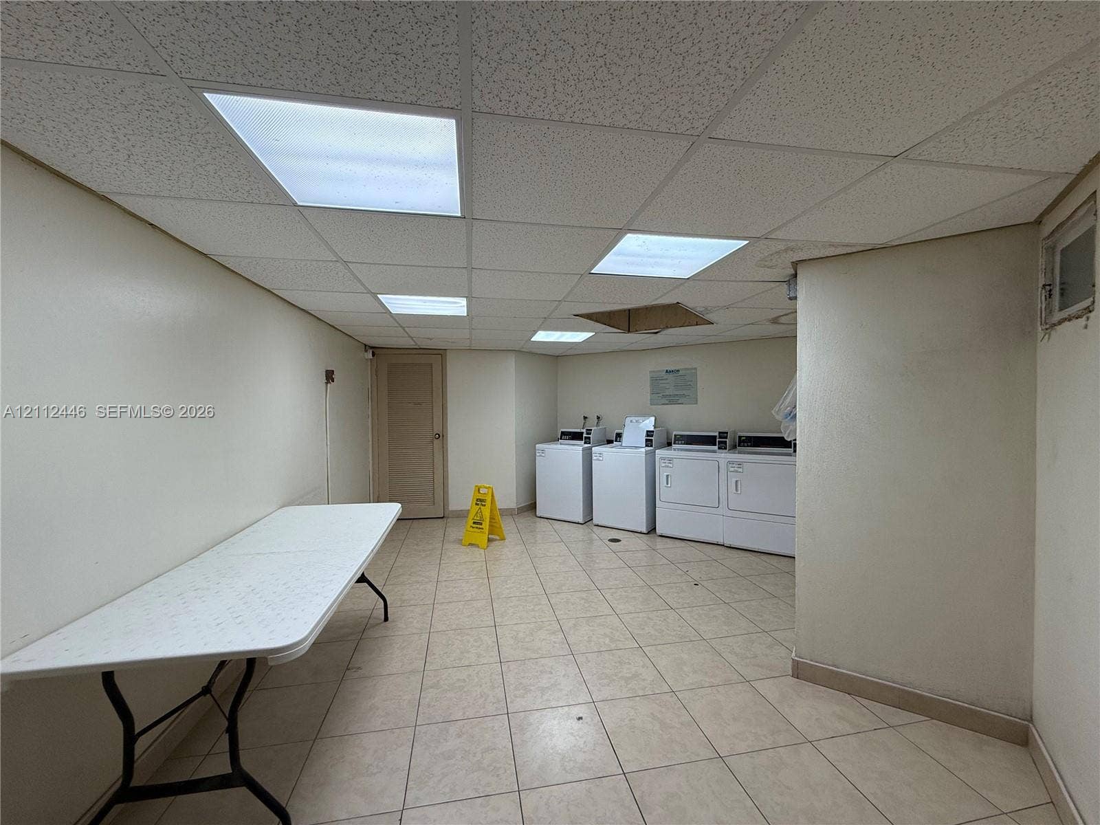 6100 S Falls Cir Drive, #411, Lauderhill, FL 33319 Laundry room featuring tile flooring, a drop ceiling with recessed panel lighting, and multiple washer and dryer units