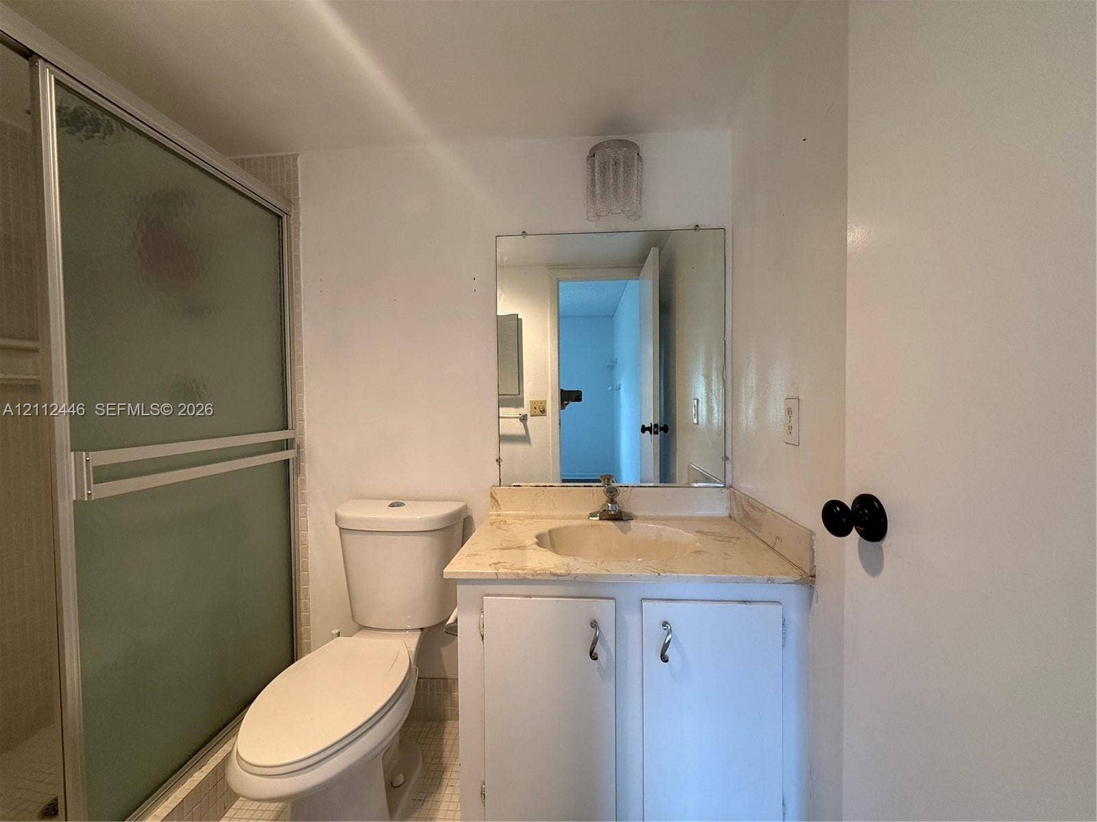 6100 S Falls Cir Drive, #411, Lauderhill, FL 33319 Bathroom featuring a stone-surface vanity with an integrated basin, a shower enclosure with a frosted sliding glass door, a wall-mounted mirror, and a crystal-style light fixture