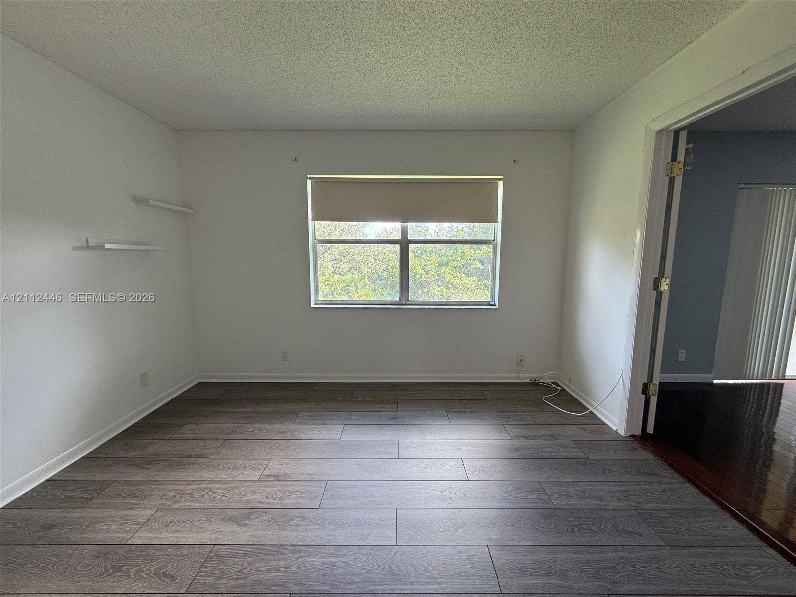 6100 S Falls Cir Drive, #411, Lauderhill, FL 33319 Interior room featuring wood-finish flooring, two wall-mounted shelves, and a single-pane window with a roller shade