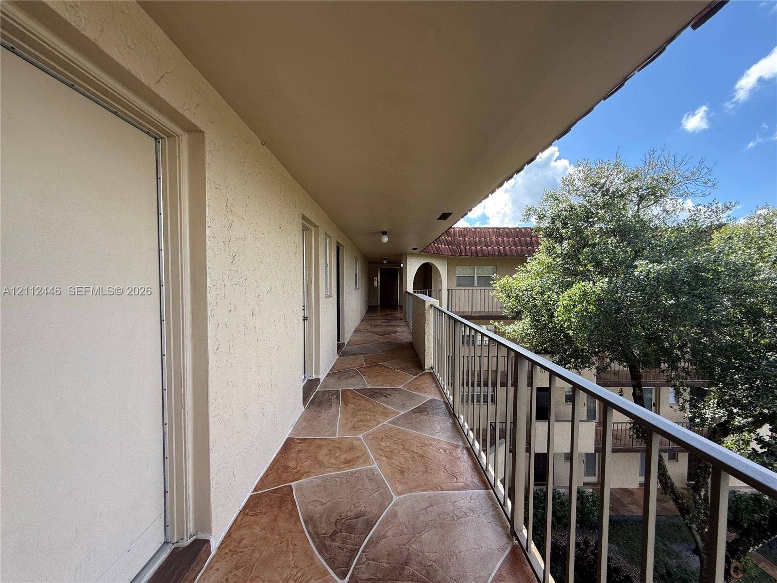 6100 S Falls Cir Drive, #411, Lauderhill, FL 33319 Exterior covered walkway featuring stamped concrete flooring, textured stucco walls, and metal railings