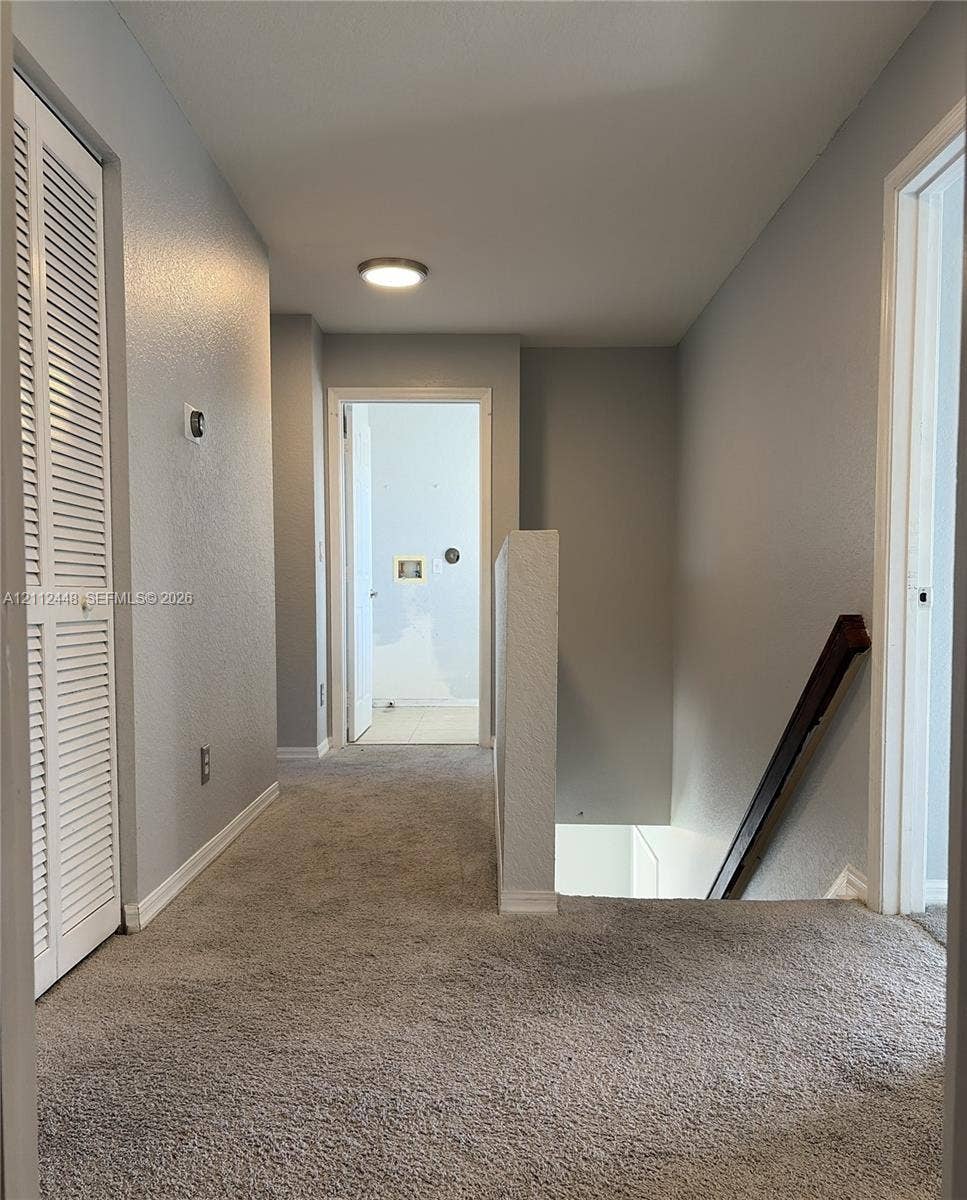 2007 SW Marblehead Way, Port St Lucie, FL 34953 Hallway featuring neutral wall paint, carpeting, built-in louvered-door closet, and wooden staircase handrail