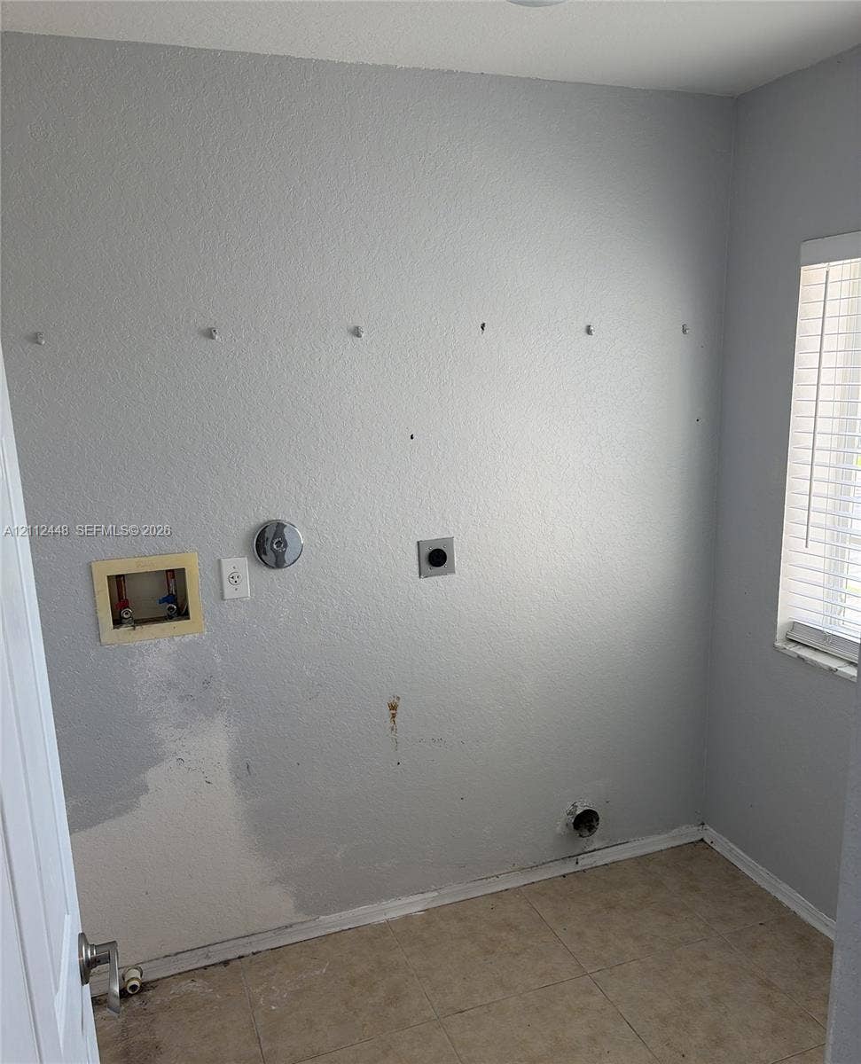 2007 SW Marblehead Way, Port St Lucie, FL 34953 Dedicated utility space featuring tile flooring, a window with horizontal blinds, and existing plumbing and electrical hookups