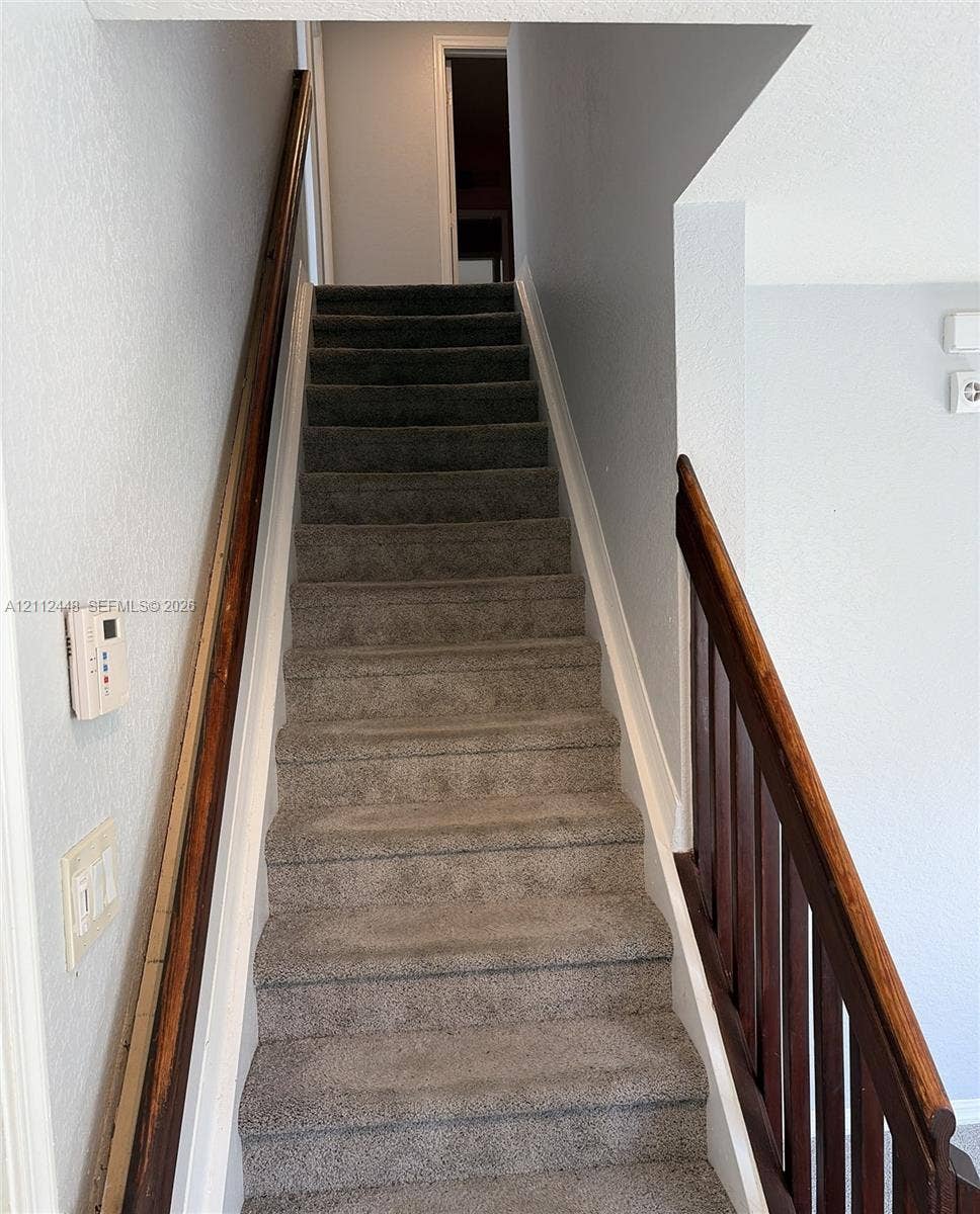 2007 SW Marblehead Way, Port St Lucie, FL 34953 Staircase featuring neutral-toned carpeting, dark stained wood handrails, and vertical balusters