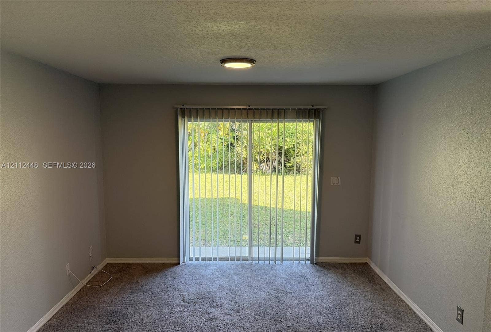 2007 SW Marblehead Way, Port St Lucie, FL 34953 Interior space featuring textured walls, neutral wall-to-wall carpeting, and a glass sliding door with vertical blinds