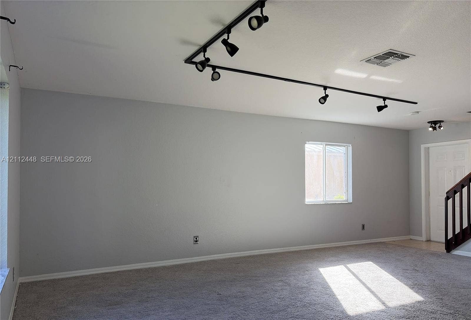 2007 SW Marblehead Way, Port St Lucie, FL 34953 Interior space featuring wall-to-wall carpeting, adjustable black track lighting, and a multi-panel door with a dark-toned handrail