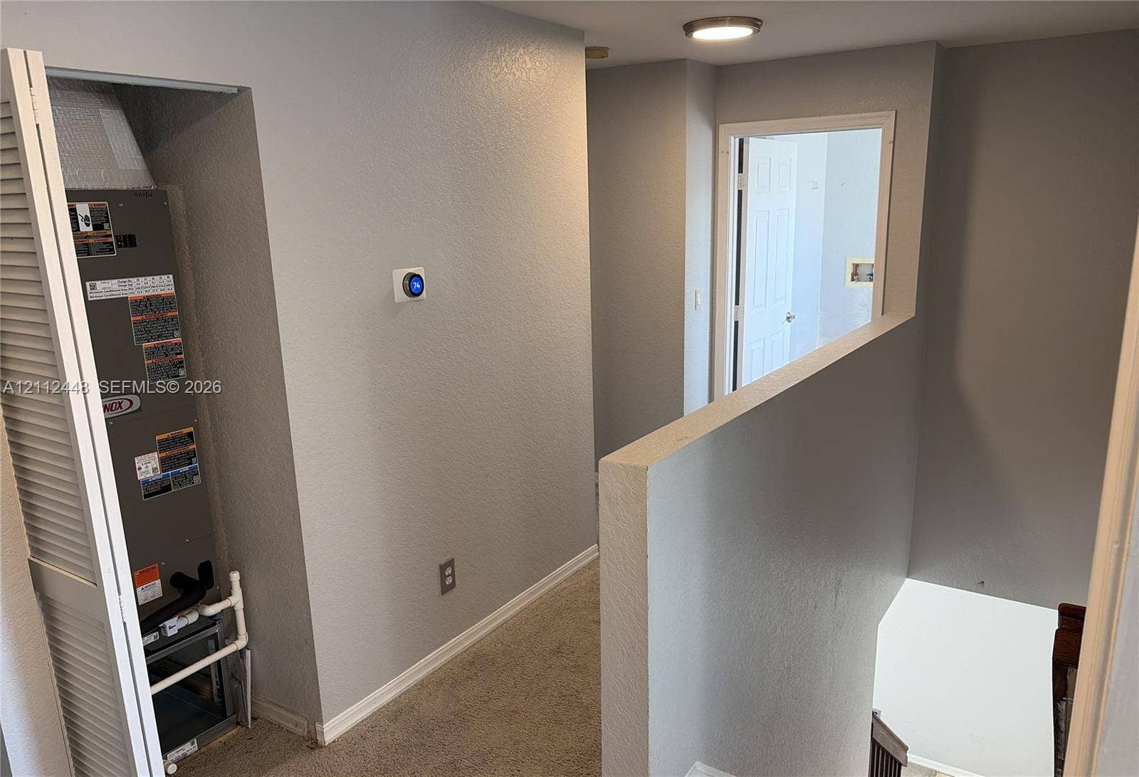 2007 SW Marblehead Way, Port St Lucie, FL 34953 Interior hall featuring a digital programmable thermostat, louvered closet door concealing mechanical systems, and flush-mount ceiling lighting