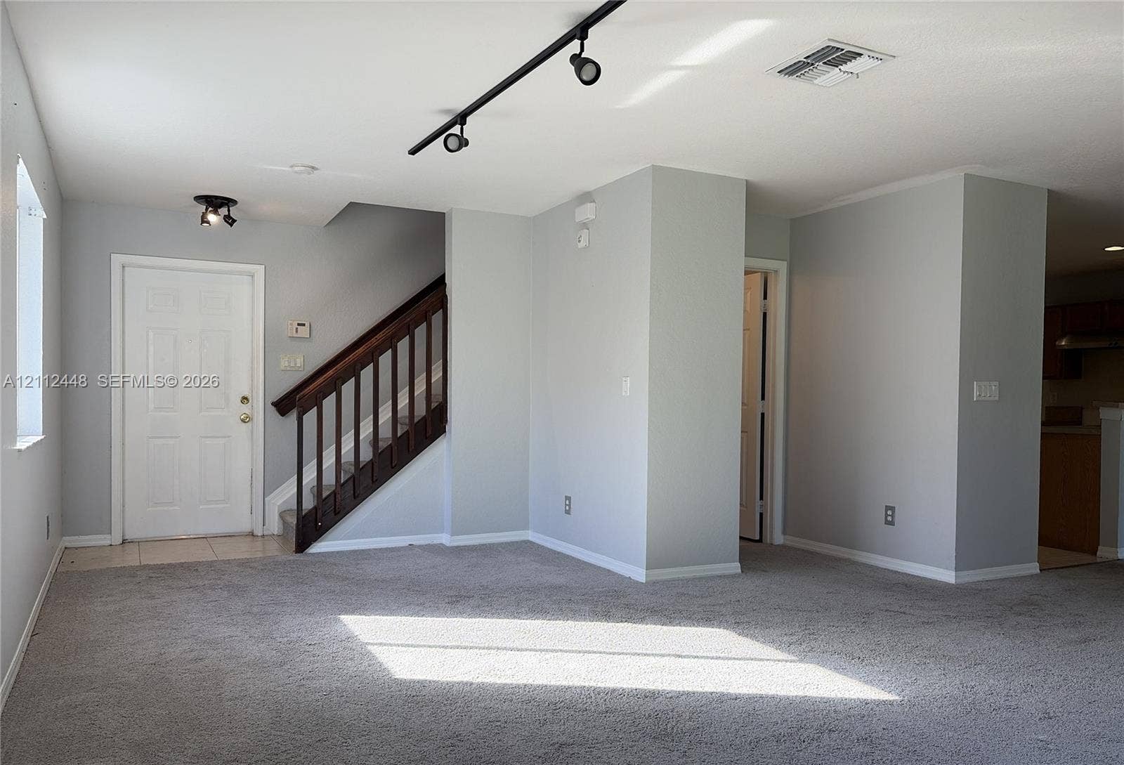 2007 SW Marblehead Way, Port St Lucie, FL 34953 Interior space featuring neutral-toned wall paint, neutral carpeting, track lighting, and a staircase with a dark wood railing