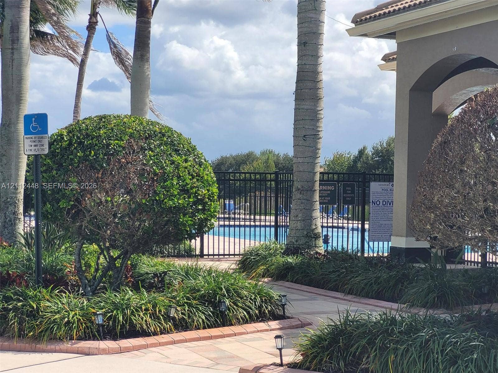 2007 SW Marblehead Way, Port St Lucie, FL 34953 Swimming pool enclosed by a metal fence, bordered by stone-paver walkways, mature palm trees, and manicured landscaping