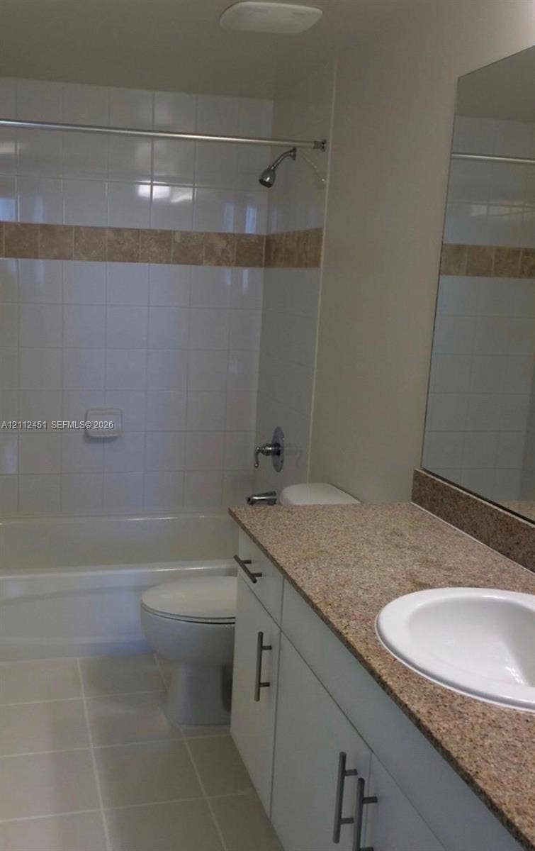 Bathroom featuring a vanity with stone-finish countertop, white cabinetry with metallic hardware, integrated sink, and a shower-tub combination with tiled walls and decorative accent band