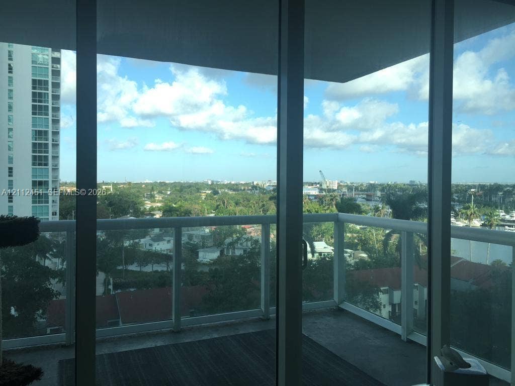 Covered balcony featuring full-height glass sliding doors, white metal railings, and concrete flooring