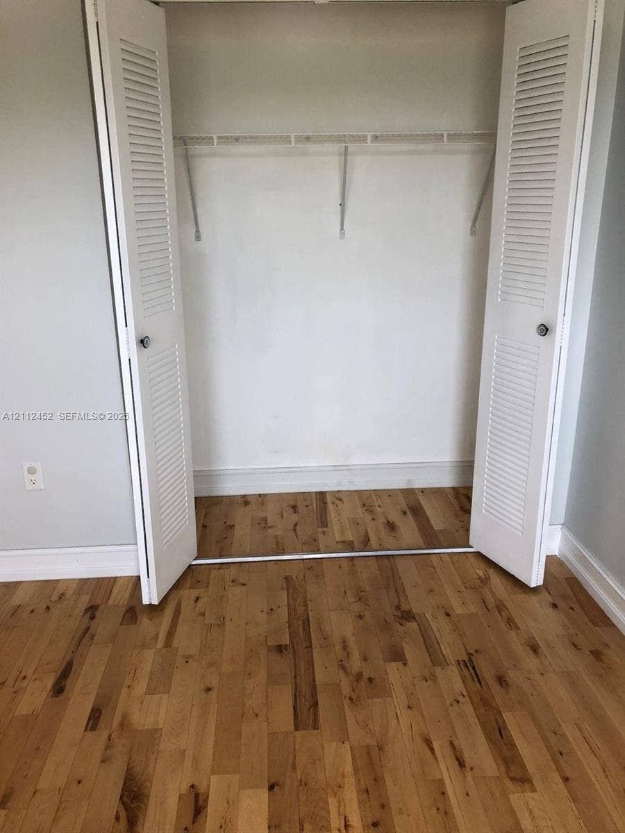 Closet featuring white louvered bifold doors and a metal shelving rod, set against wood-finish flooring