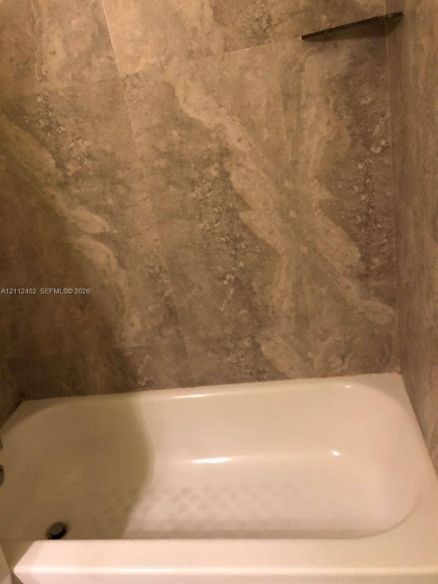 Bathtub with a white finish, surrounded by floor-to-ceiling large-format stone-finish wall tiles and a built-in triangular corner shelf