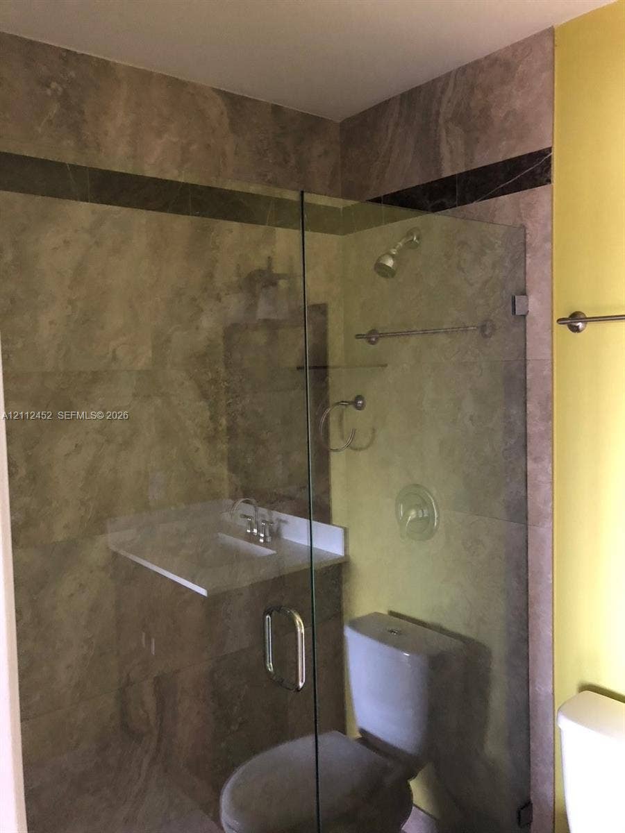 Walk-in shower enclosure with glass door, stone-tile surround, integrated accent border, chrome rainfall showerhead, and wall-mounted metal hardware