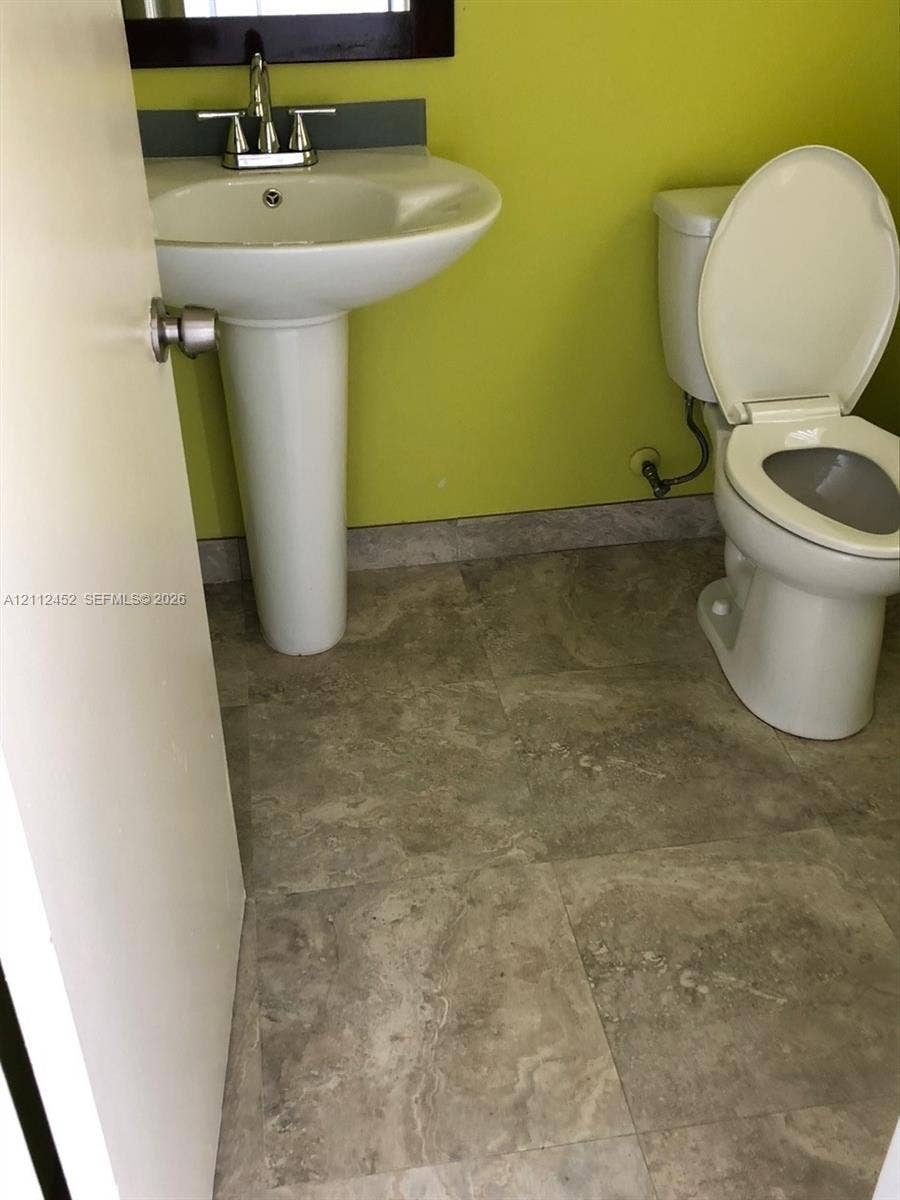 White pedestal sink with chrome faucet, stone-finish tile flooring, and a two-piece porcelain toilet