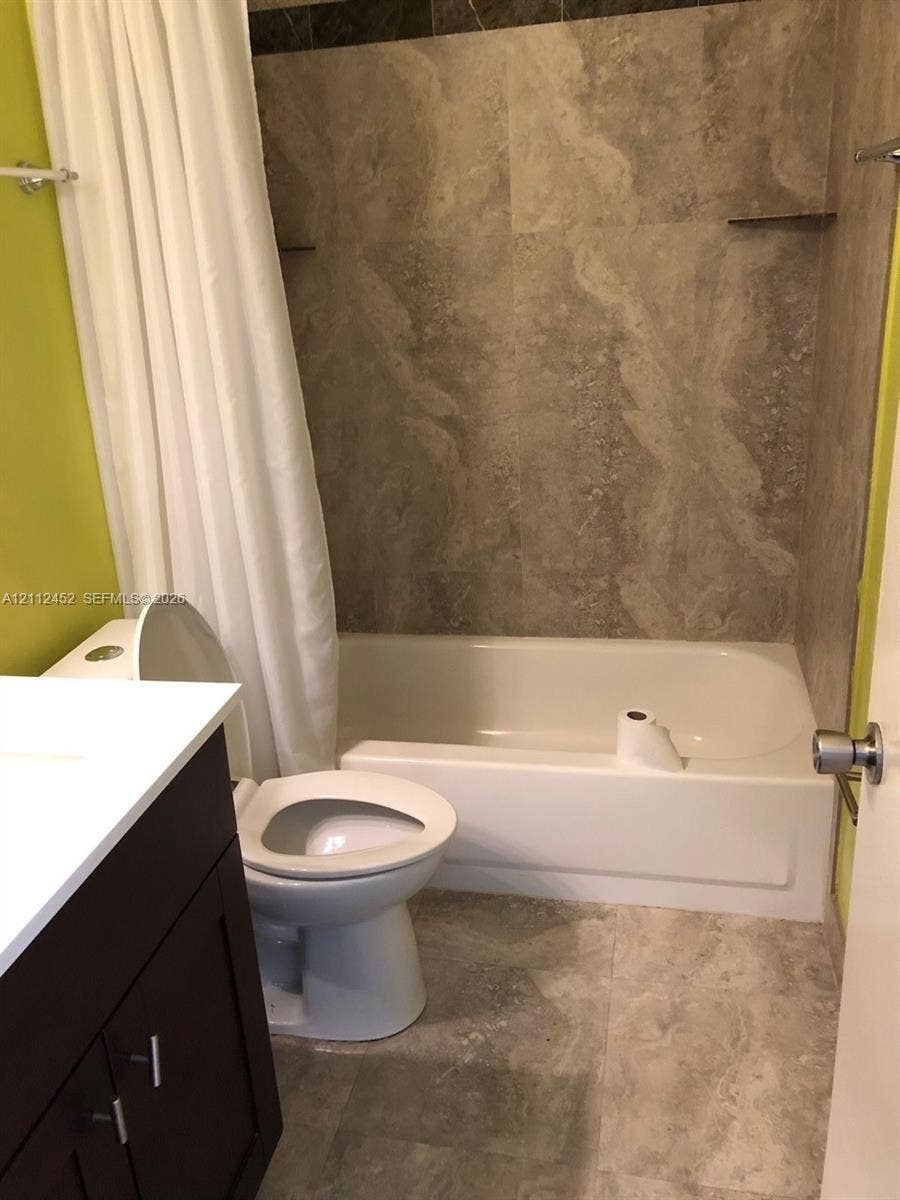 Bathroom featuring a vanity with white countertop, stone-finish tile shower surround, and stone-finish floor tiling