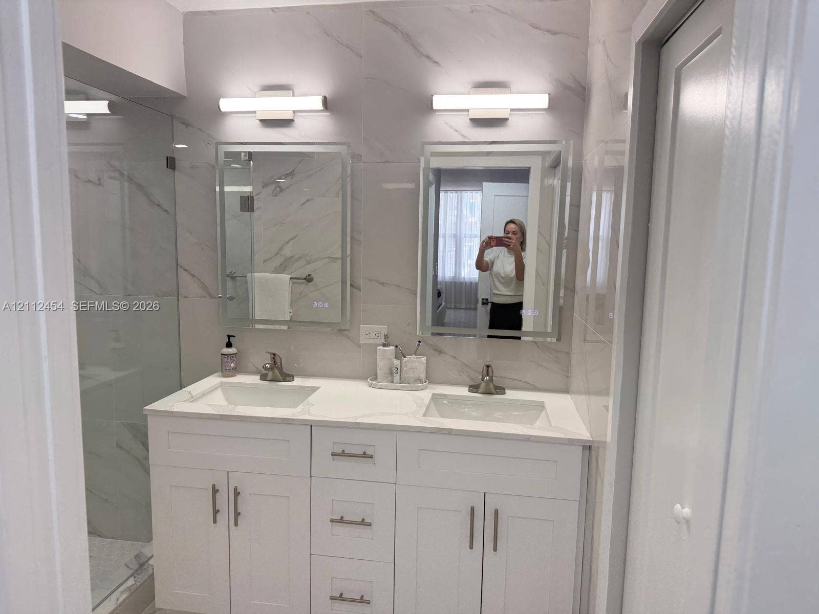 3800 S Ocean Drive, #1601, Hollywood, Hollywood, FL 33019 Double vanity featuring white shaker-style cabinetry, white stone-composite countertops, integrated rectangular sinks, and illuminated wall-mounted mirrors with large-format tile surround