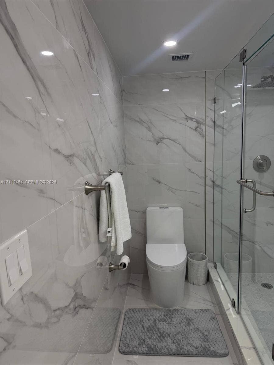 3800 S Ocean Drive, #1601, Hollywood, Hollywood, FL 33019 Full-height, stone-finish wall tiling, glass-enclosed shower stall with polished metal fixtures, and dual-flush toilet
