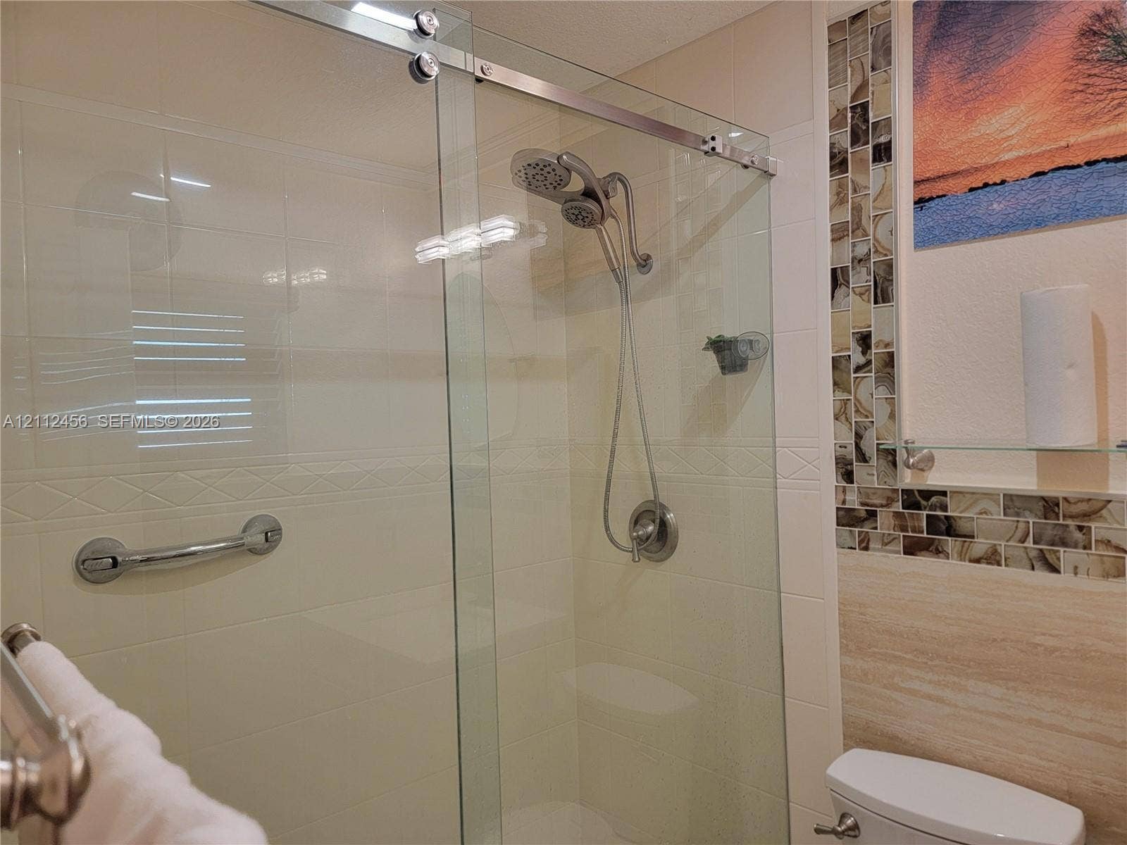 3961 NW 110th Avenue, #3961, Coral Springs, Coral Springs, FL 33065 Shower stall featuring a glass sliding door, metallic handheld shower fixture, integrated grab bar, and neutral wall tiling with decorative mosaic accent strips