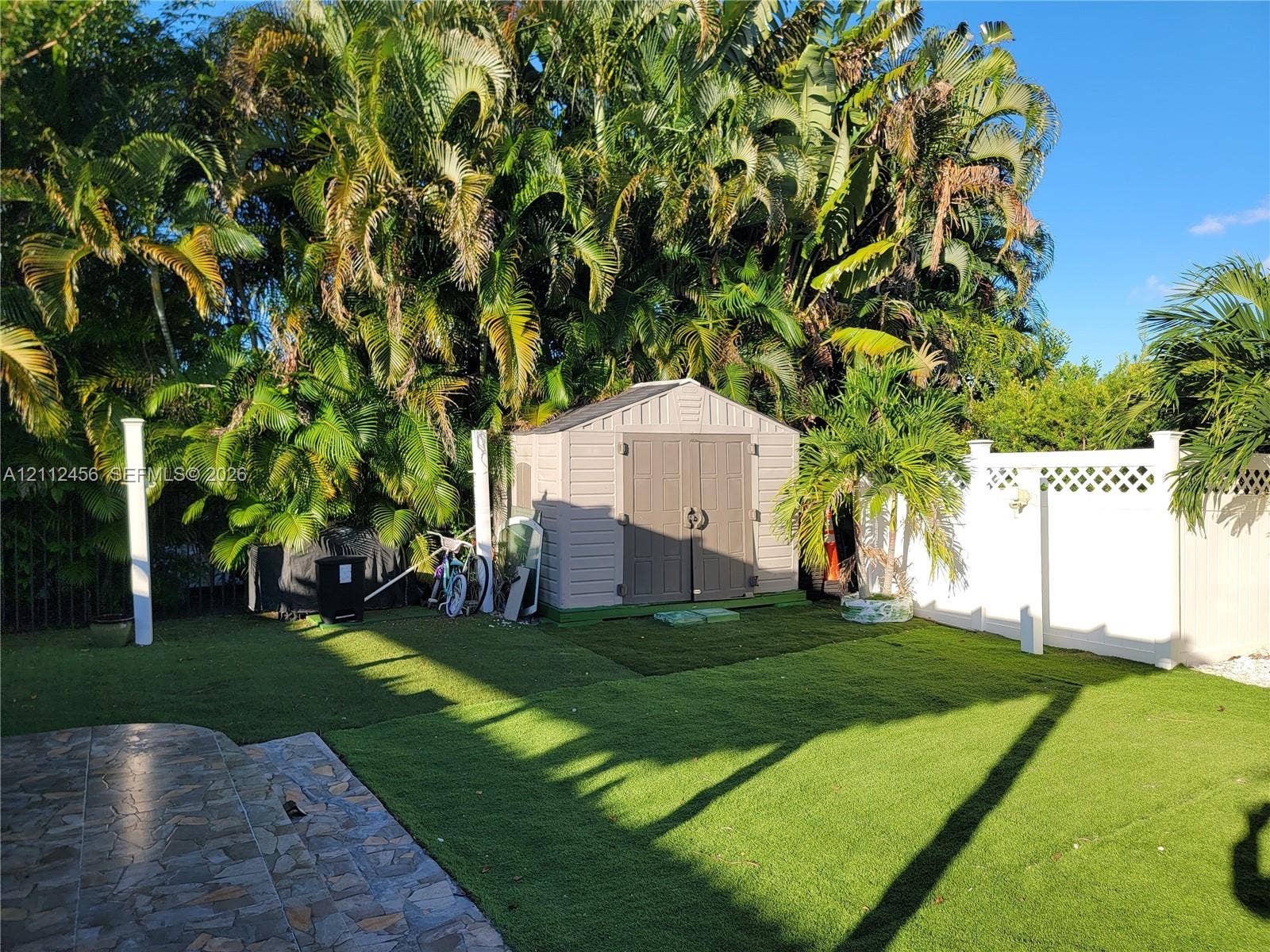 3961 NW 110th Avenue, #3961, Coral Springs, Coral Springs, FL 33065 Rear exterior featuring synthetic turf lawn, white vinyl privacy fencing with lattice detail, stone-paver patio, and exterior storage shed