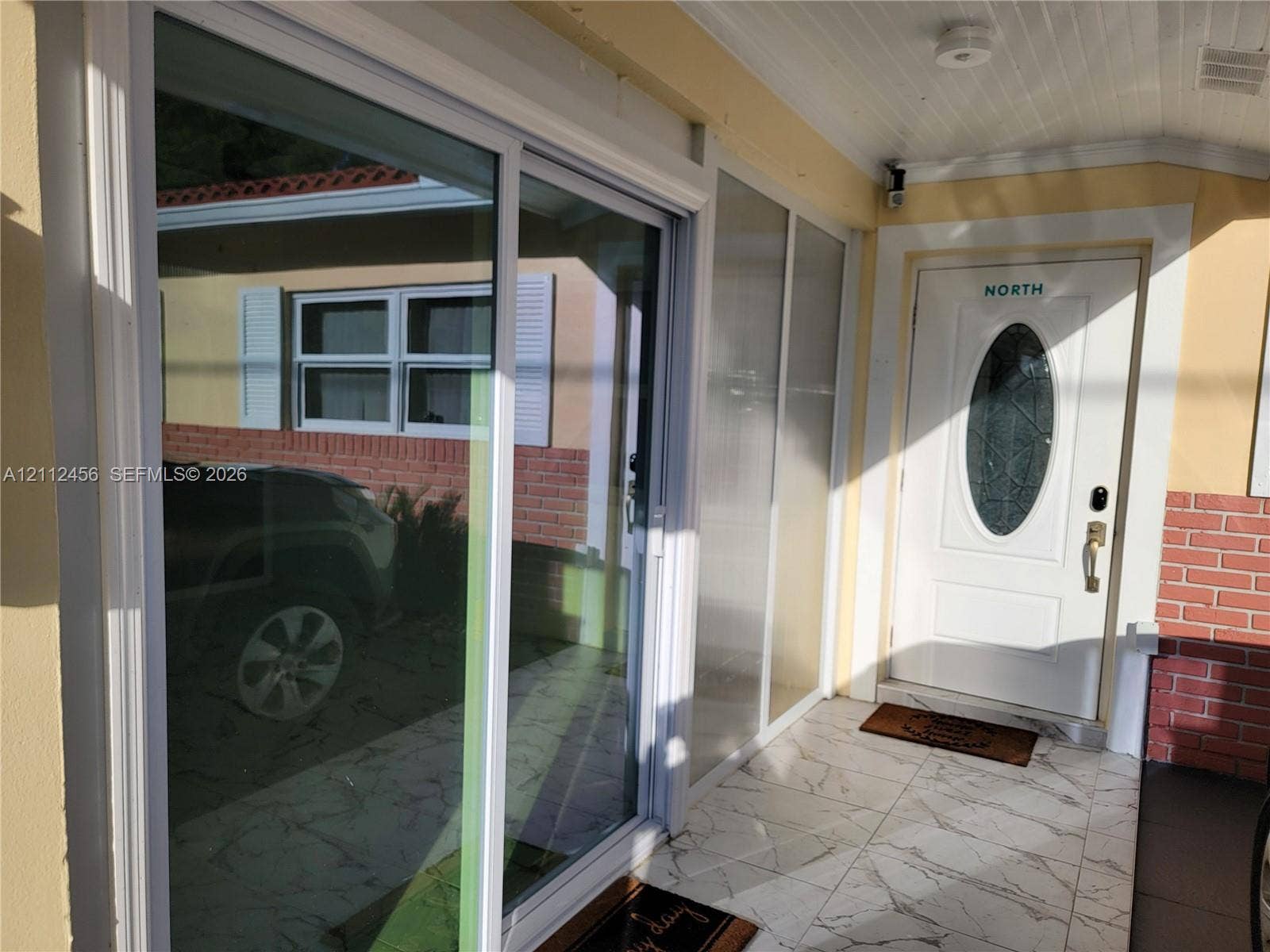 3961 NW 110th Avenue, #3961, Coral Springs, Coral Springs, FL 33065 Covered entryway featuring stone-finish floor tile, a white entry door with an oval glass insert, and full-length glass sliding doors