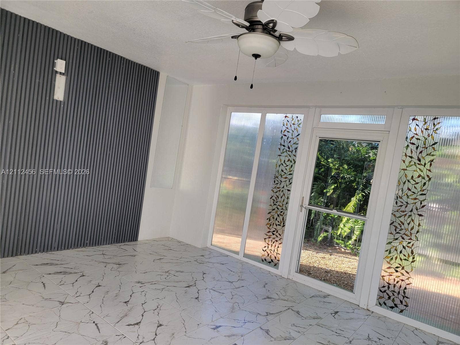 3961 NW 110th Avenue, #3961, Coral Springs, Coral Springs, FL 33065 Enclosed space featuring large-format tile flooring, a corrugated metal accent wall, and a ceiling fan with leaf-patterned blades