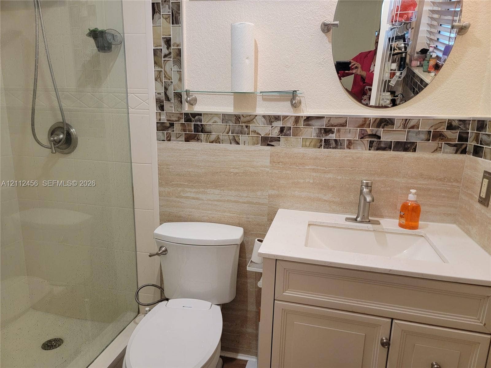 3961 NW 110th Avenue, #3961, Coral Springs, Coral Springs, FL 33065 Bathroom featuring a vanity with a white countertop and rectangular undermount sink, stone-finish wall tiling, decorative mosaic tile accents, a glass-enclosed shower, and an oval wall-mounted mirror
